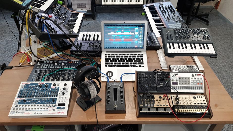 A modern recording studio setup with audio equipment, synthesizers, and a laptop for music production.